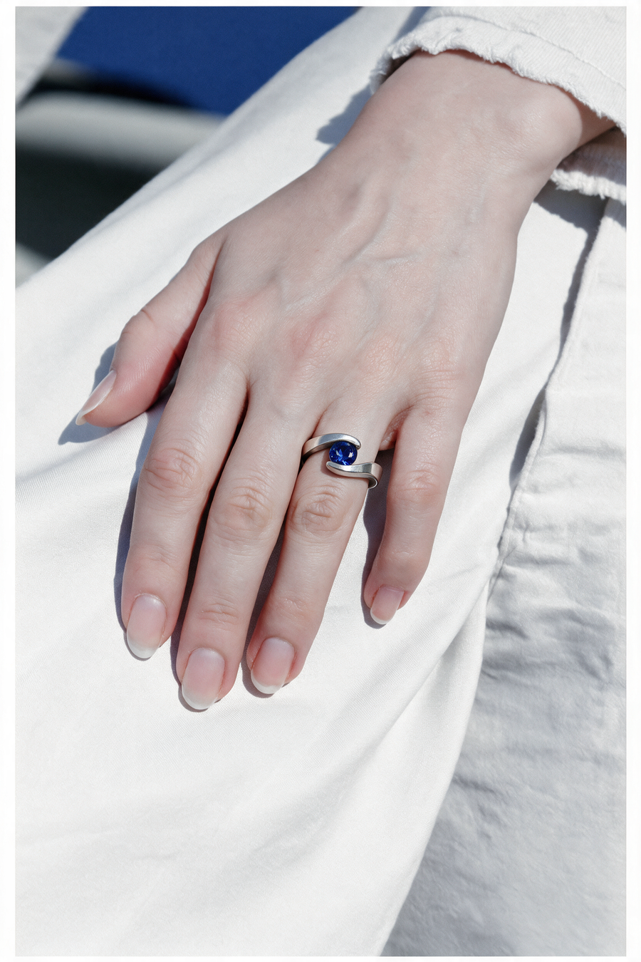 Embrace Ring in sterling silver with a blue stone on a hand resting on white cotton