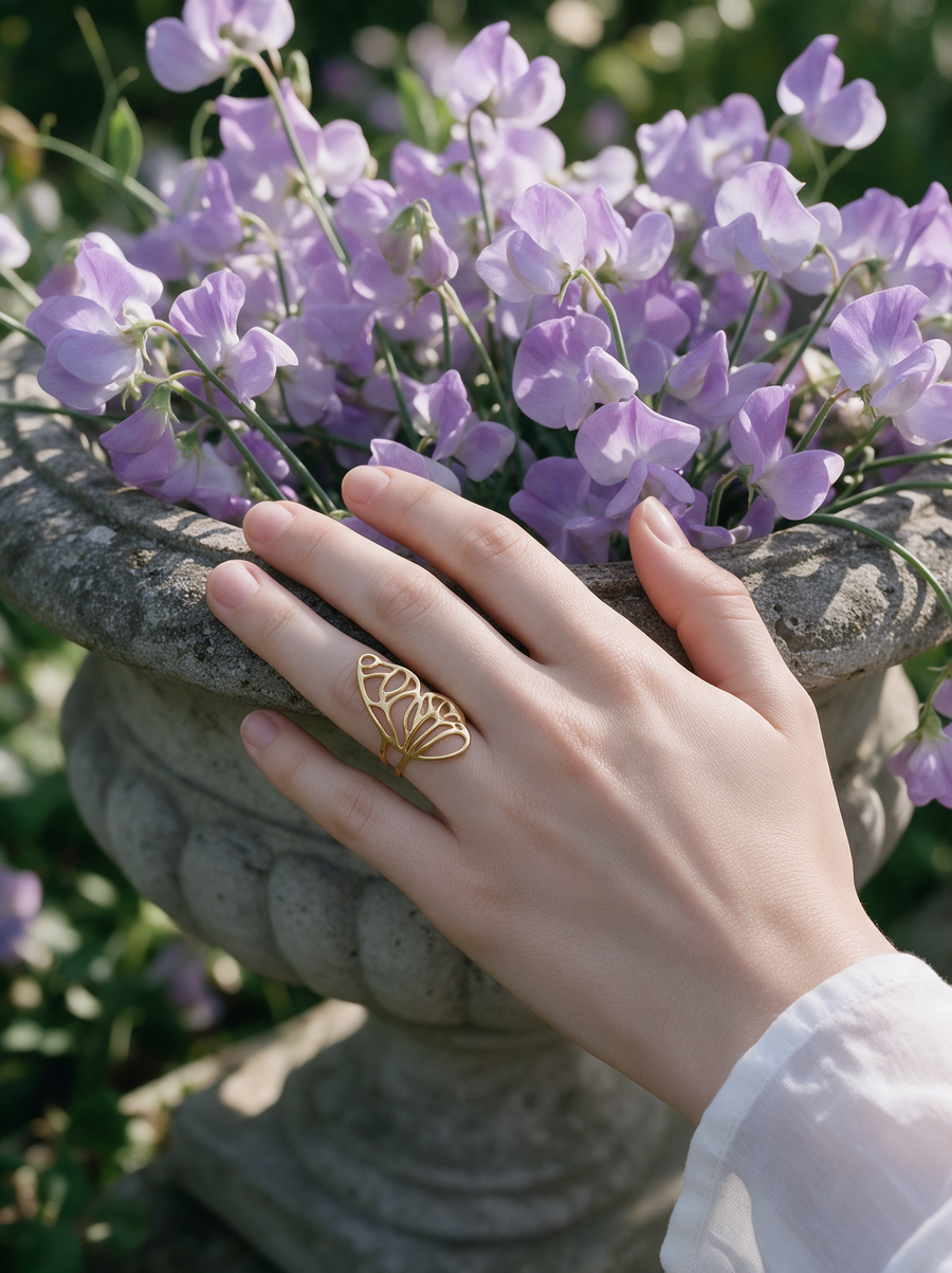 Butterfly Wing Ring in 18K gold vermeil on a hand resting on a stone urn of purple sweet peas