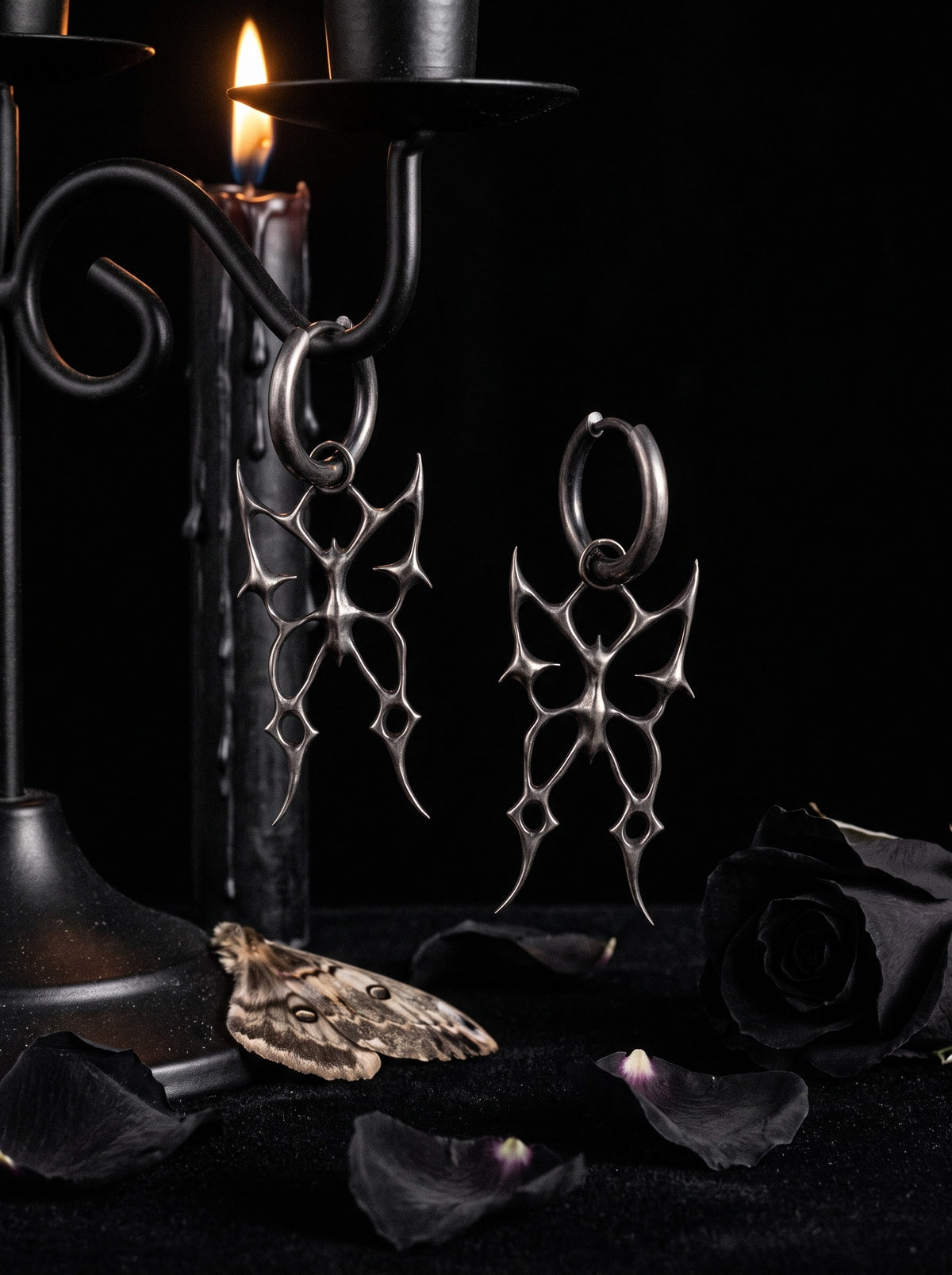 Barbed Butterfly Earrings in oxidised sterling silver on a black candle stand with dark roses