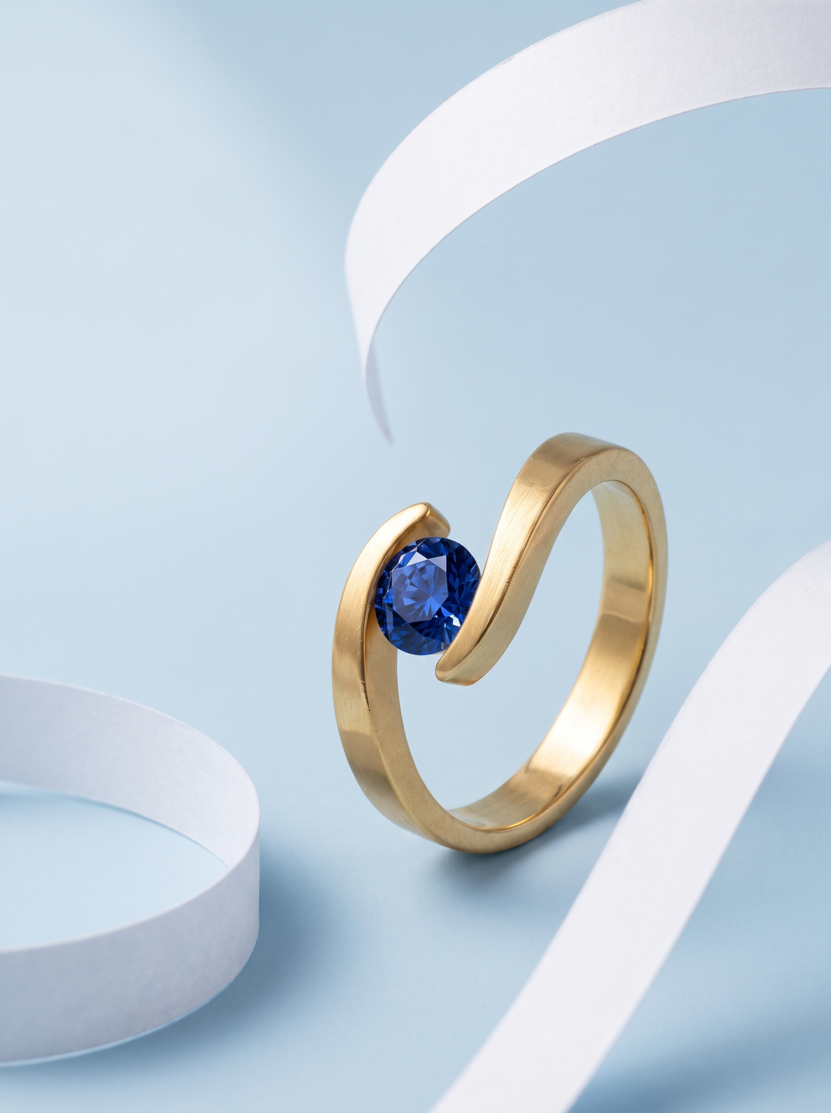 Embrace Ring in 18K gold vermeil with a blue stone on pale blue with curls of white paper