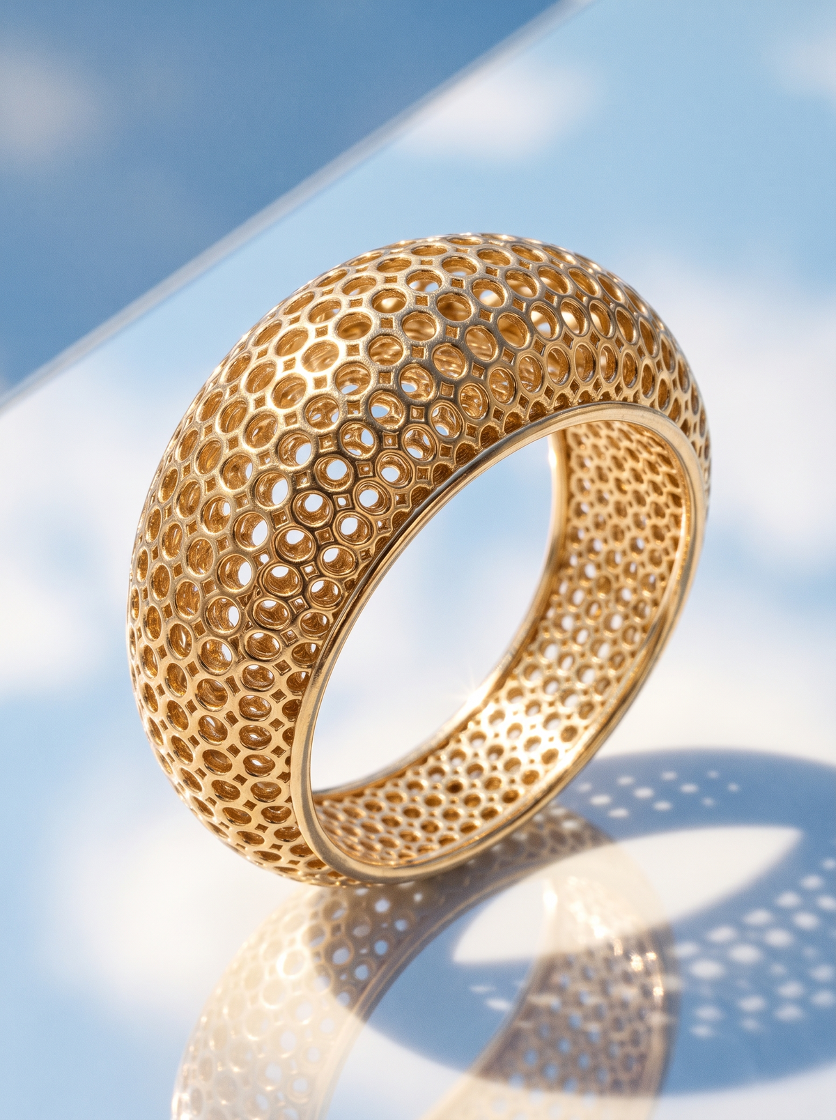 The Mesh Ring in 18K gold vermeil on a mirror reflecting blue sky and clouds