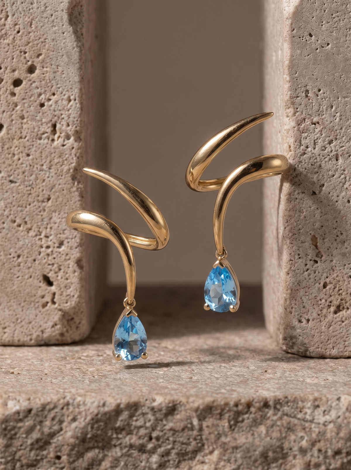 Spiral Drop Earrings in 18K gold vermeil with light blue teardrop stones on travertine