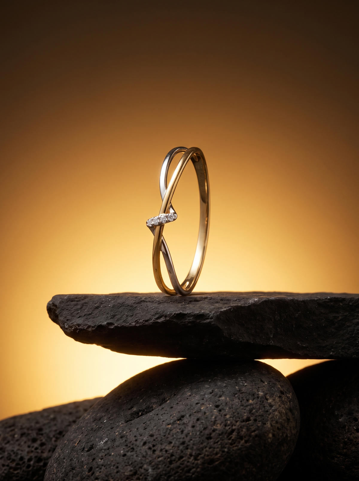 Cinch Ring in two-tone gold and silver standing on a dark stone slab against a warm amber glow