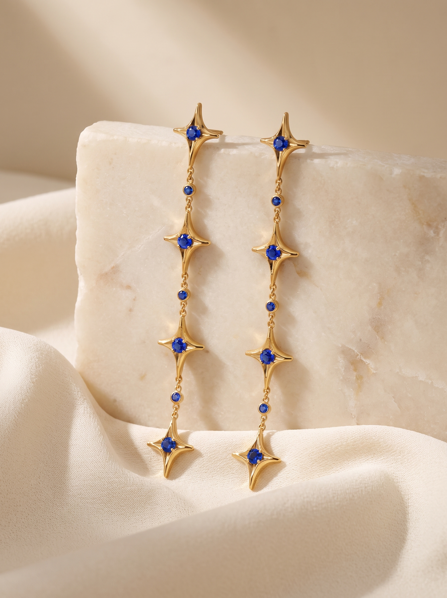 Star Chain Earrings in 18K gold vermeil with blue stones draped over a marble block on cream silk