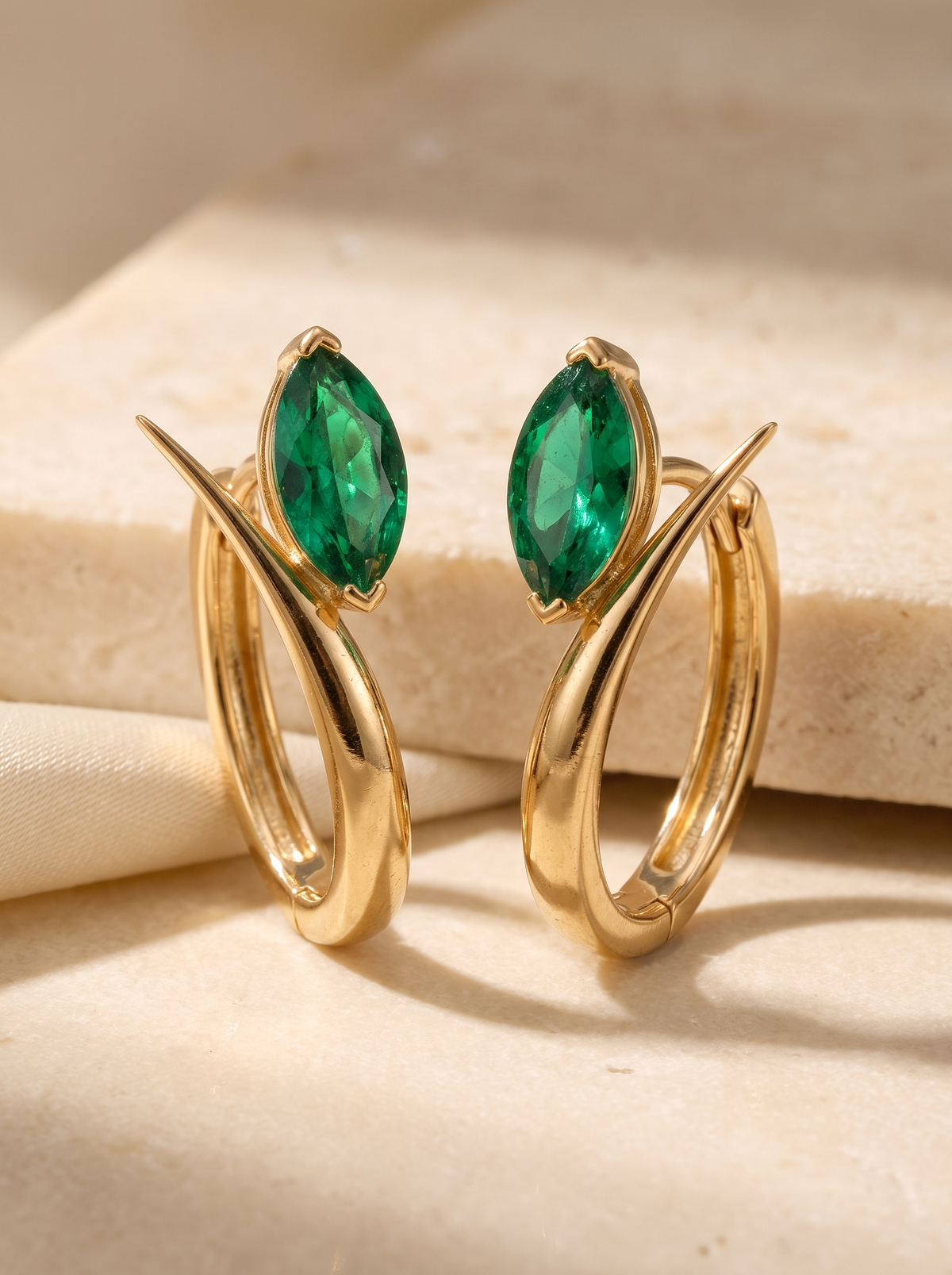 Leaf Hoops in 18K gold vermeil with green marquise stones on sunlit travertine