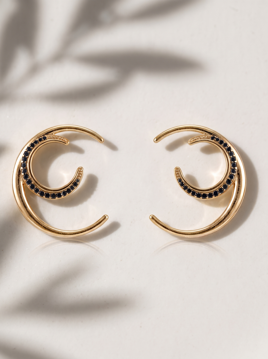 Crescent Moon Hoops in 18K gold vermeil with black stones on cream under soft leaf shadows