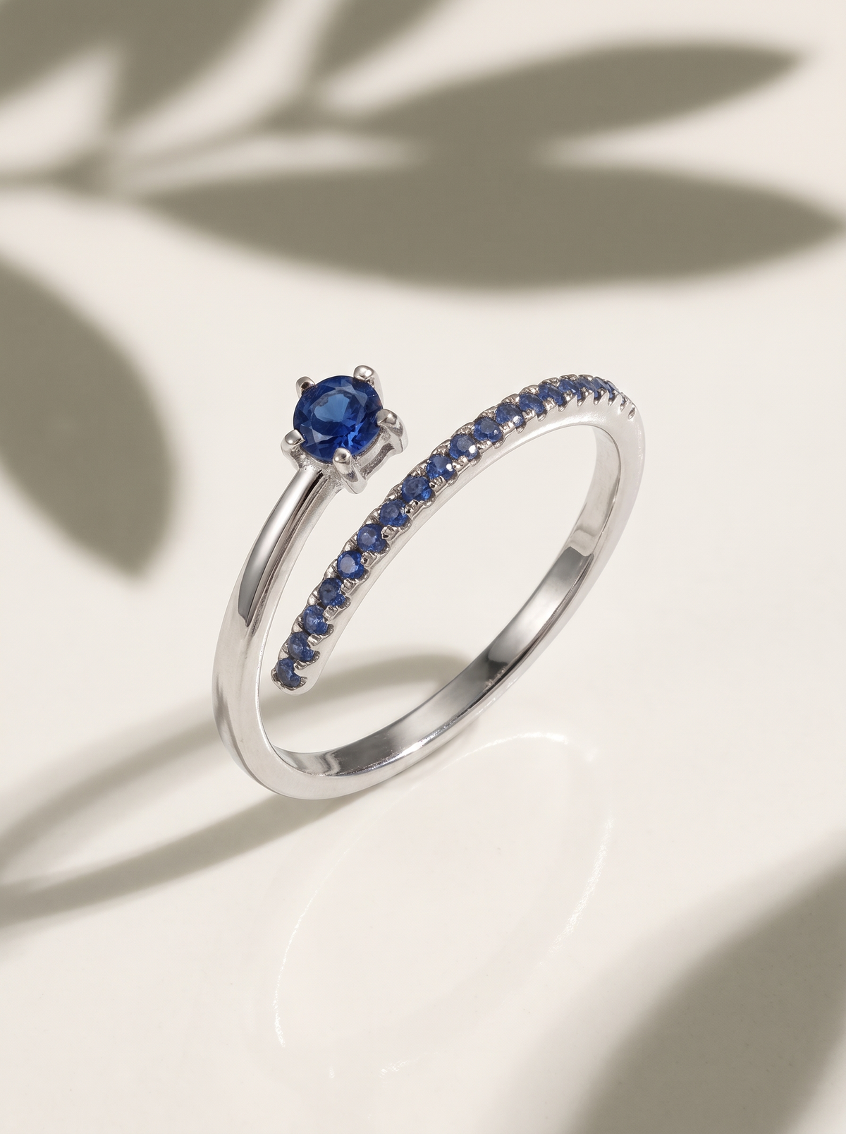 Comet Ring in sterling silver with a blue stone and blue pavé trail under soft leaf shadows