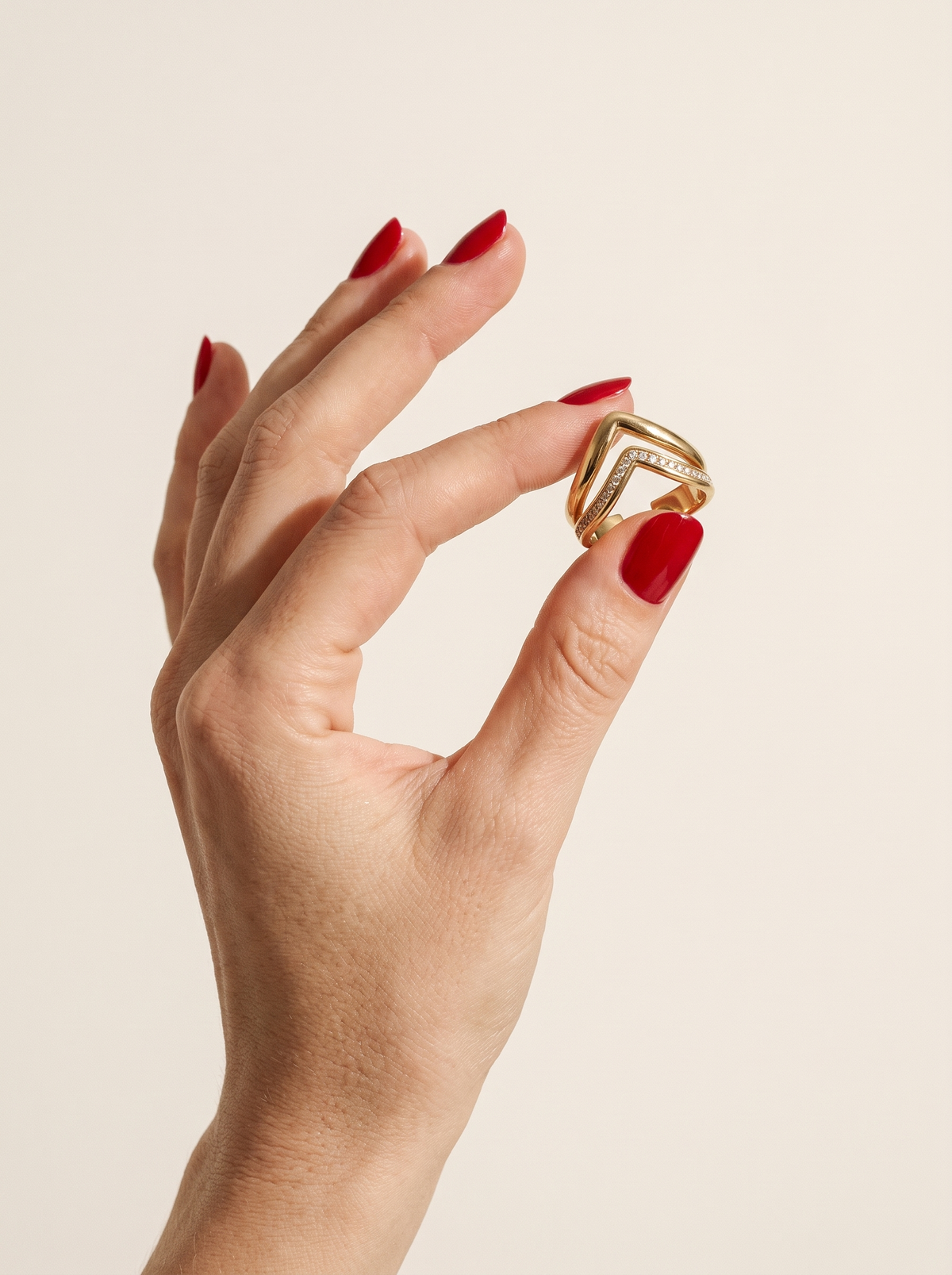 Hand with red nails holding up the Peak Ring in 18K gold vermeil against a cream backdrop