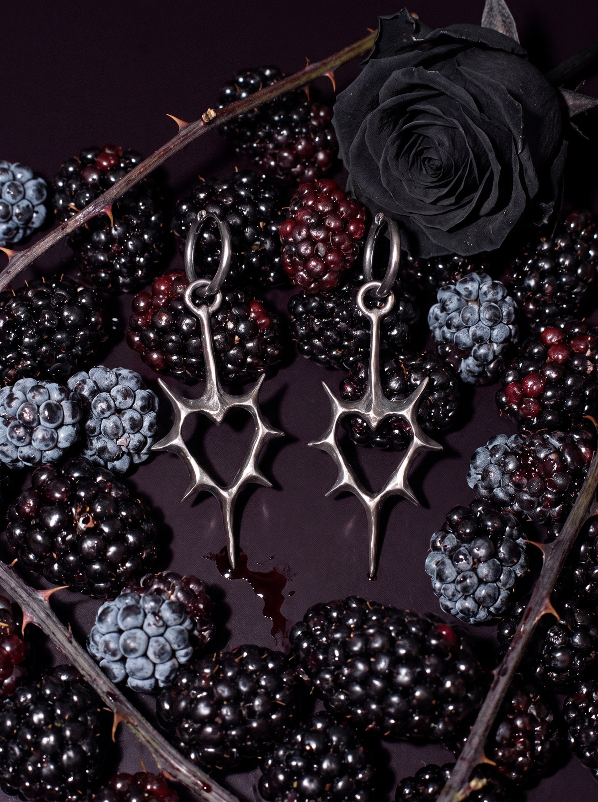 Thorn Heart Earrings in oxidised silver on blackberries beside a black rose and thorny stems