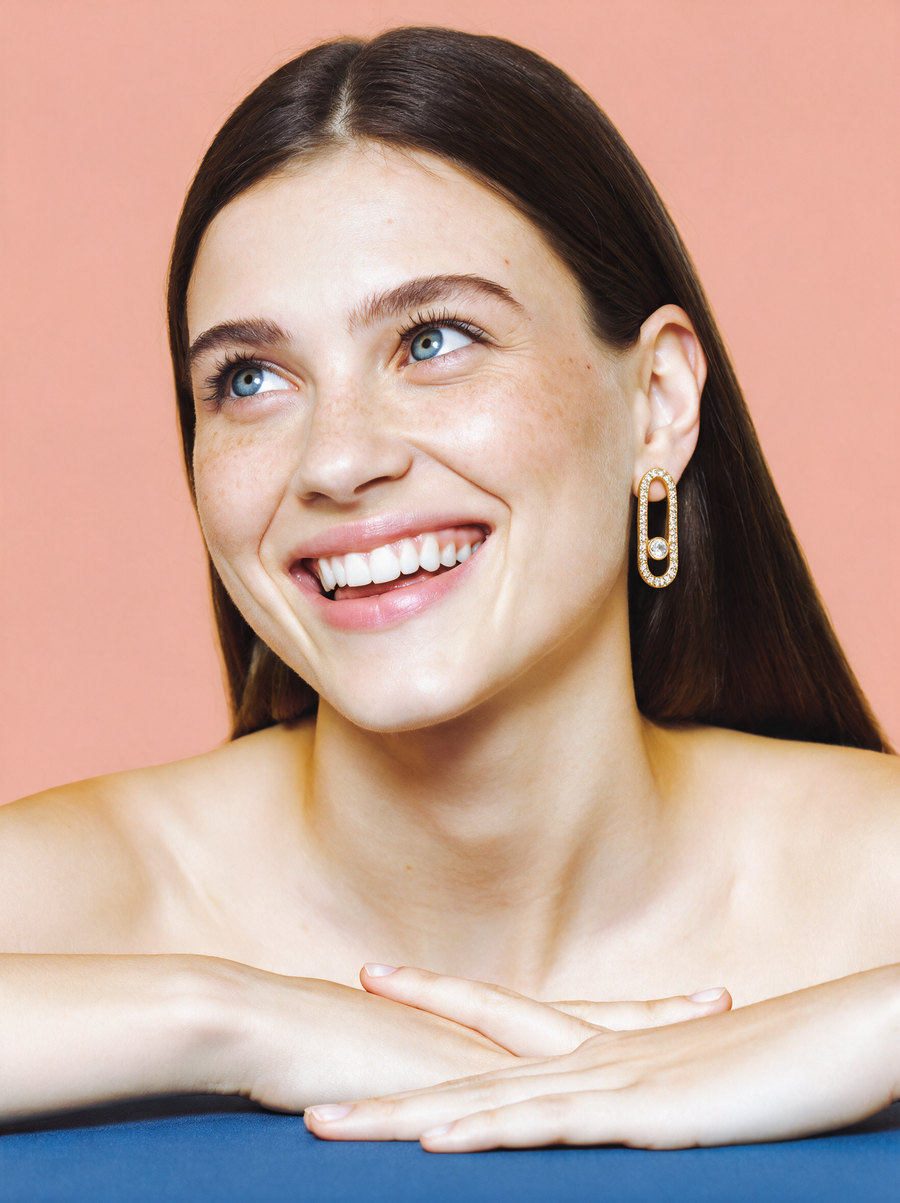 Smiling model wearing the Pavé Link Earrings in 18K gold vermeil against a peach backdrop