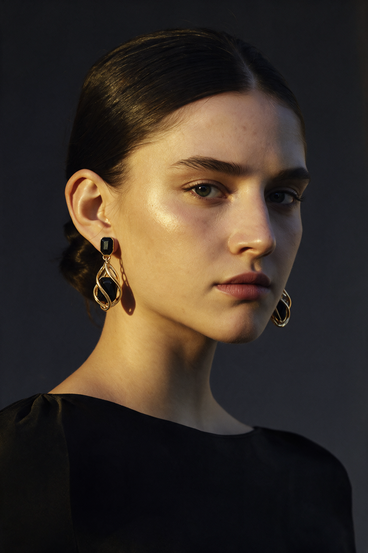 Model wearing the Black Wrap Earrings in 18K gold vermeil, hair swept back against a dark backdrop