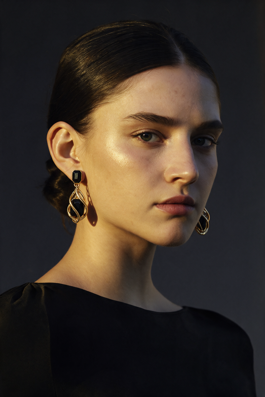 Model wearing the Black Wrap Earrings in 18K gold vermeil, hair swept back against a dark backdrop