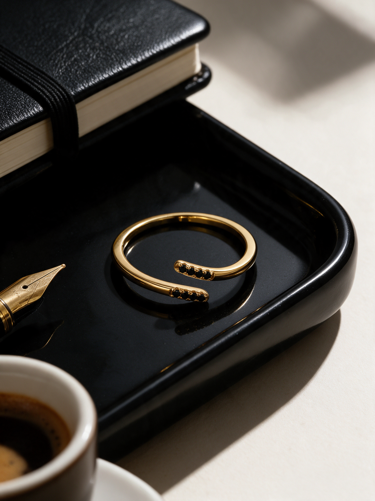 Parallel Ring in 18K gold vermeil with black stones on a black tray beside a notebook and espresso