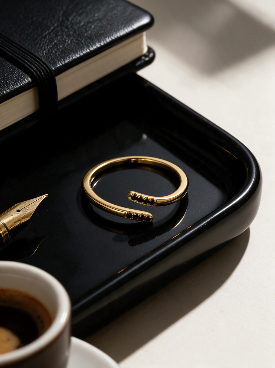 Parallel Ring in 18K gold vermeil with black stones on a black tray beside a notebook and espresso