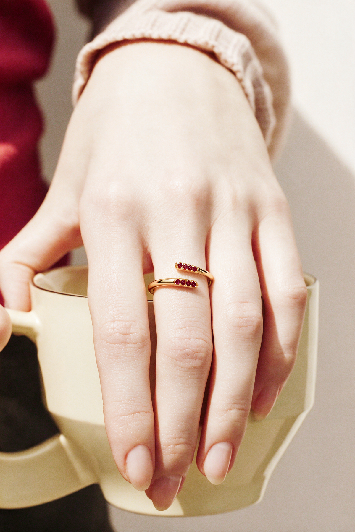 Parallel Ring in 18K gold vermeil with red stones on a hand holding a cream mug