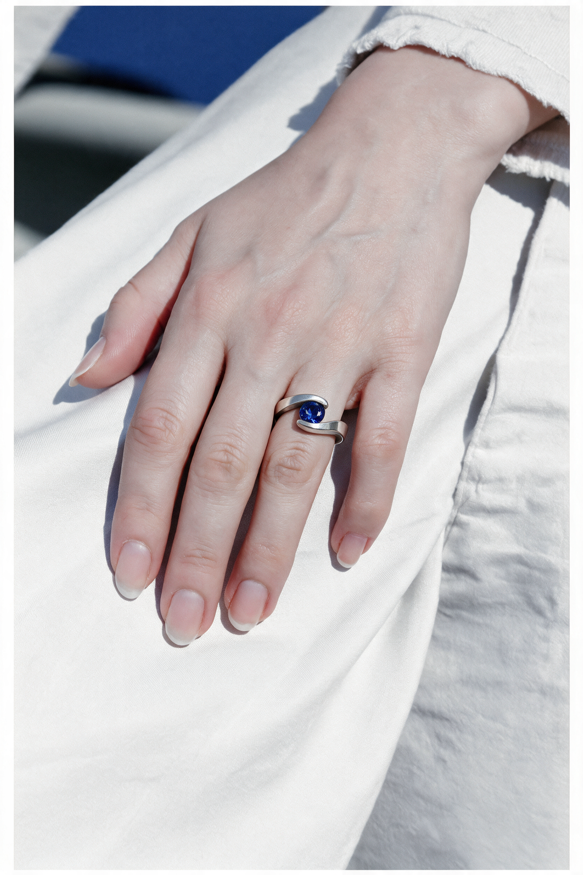 Embrace Ring in sterling silver with a blue stone on a hand resting on white cotton
