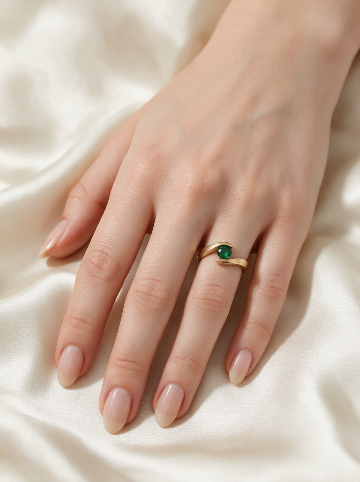 Embrace Ring in 18K gold vermeil with a green stone on a hand resting on ivory satin