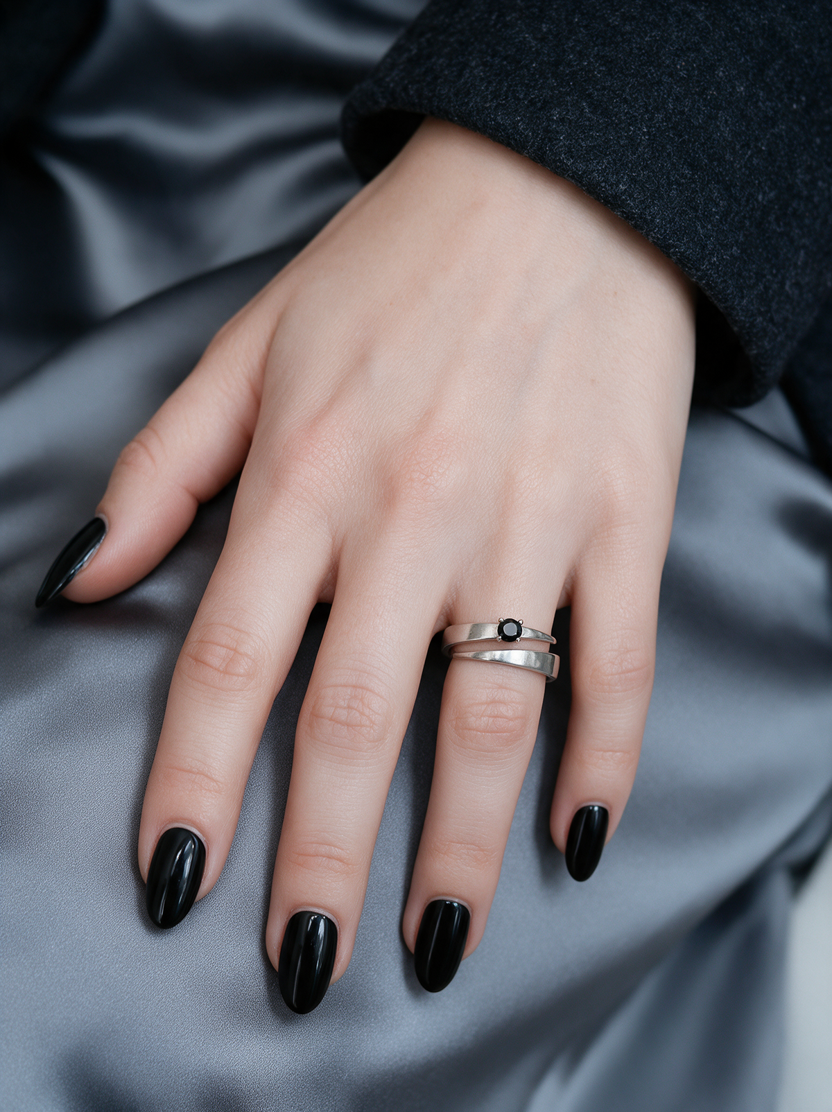 Tier Ring in sterling silver with a black stone on a hand with black nails resting on grey satin