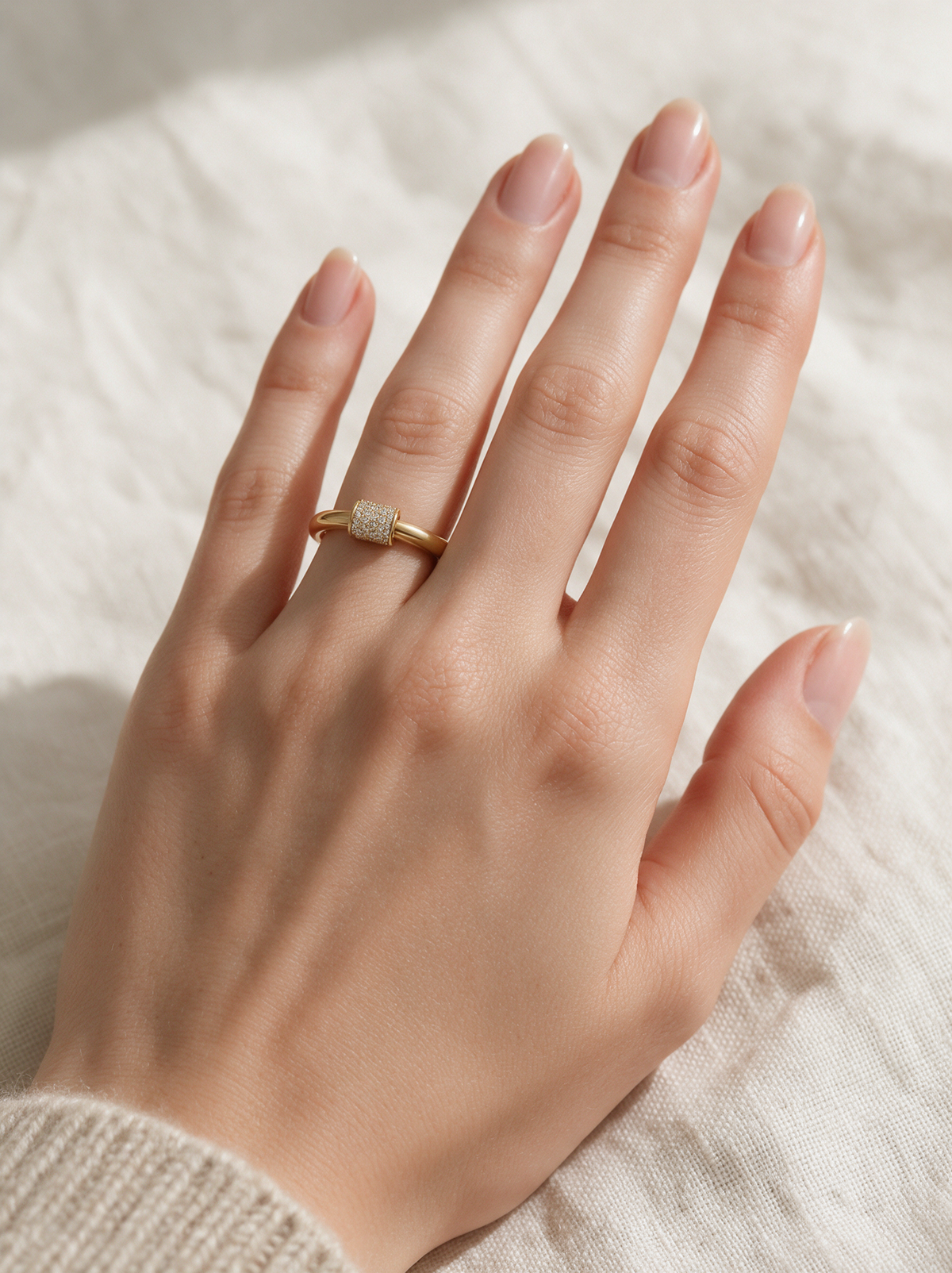Lock Ring in 18K gold vermeil with white stones on a hand resting on a cream knit throw