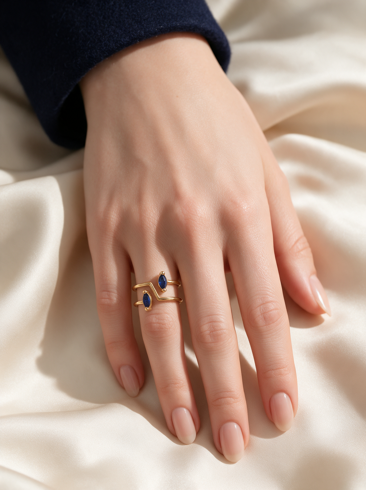 Switchback Ring in 18K gold vermeil with blue marquise stones on a hand resting on cream satin