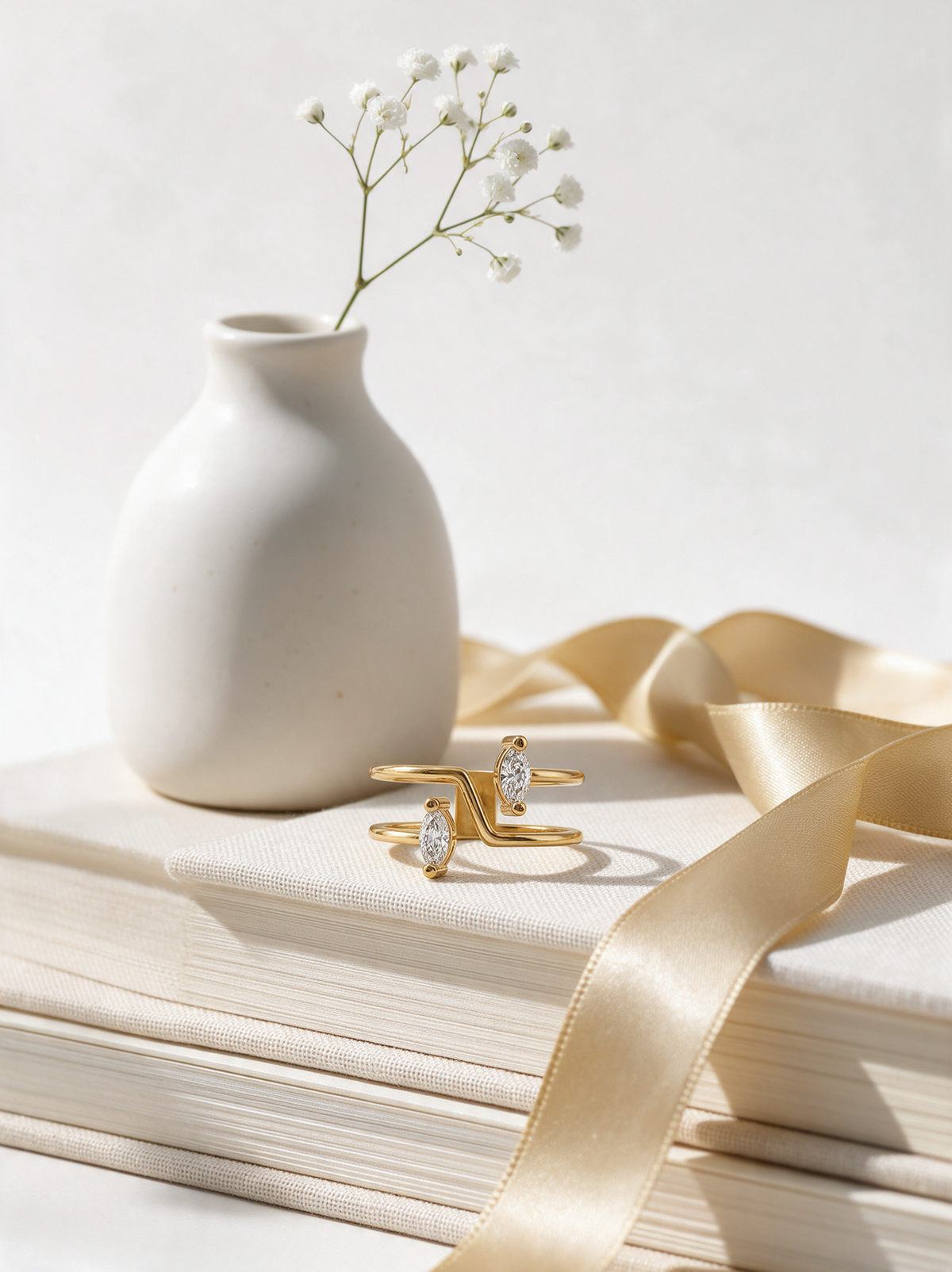 Switchback Ring in 18K gold vermeil with white stones on books beside a white vase of baby's breath