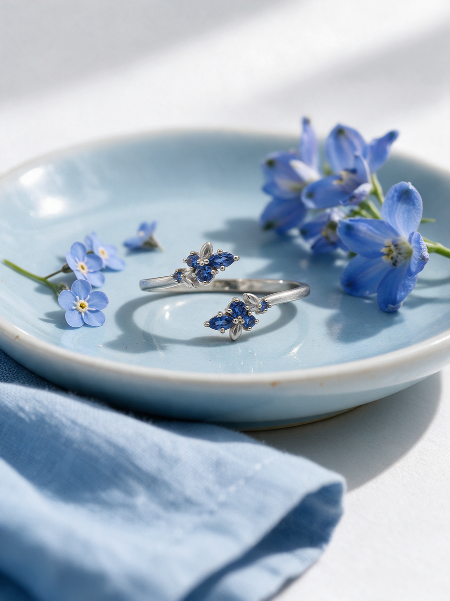 Bloom Ring in sterling silver with blue stones on a pale blue plate with blue flowers and linen