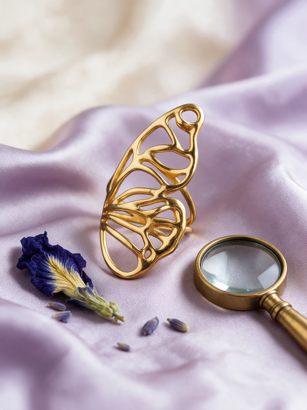 Butterfly Wing Ring in 18K gold vermeil on lilac satin beside a magnifying glass and a blue flower