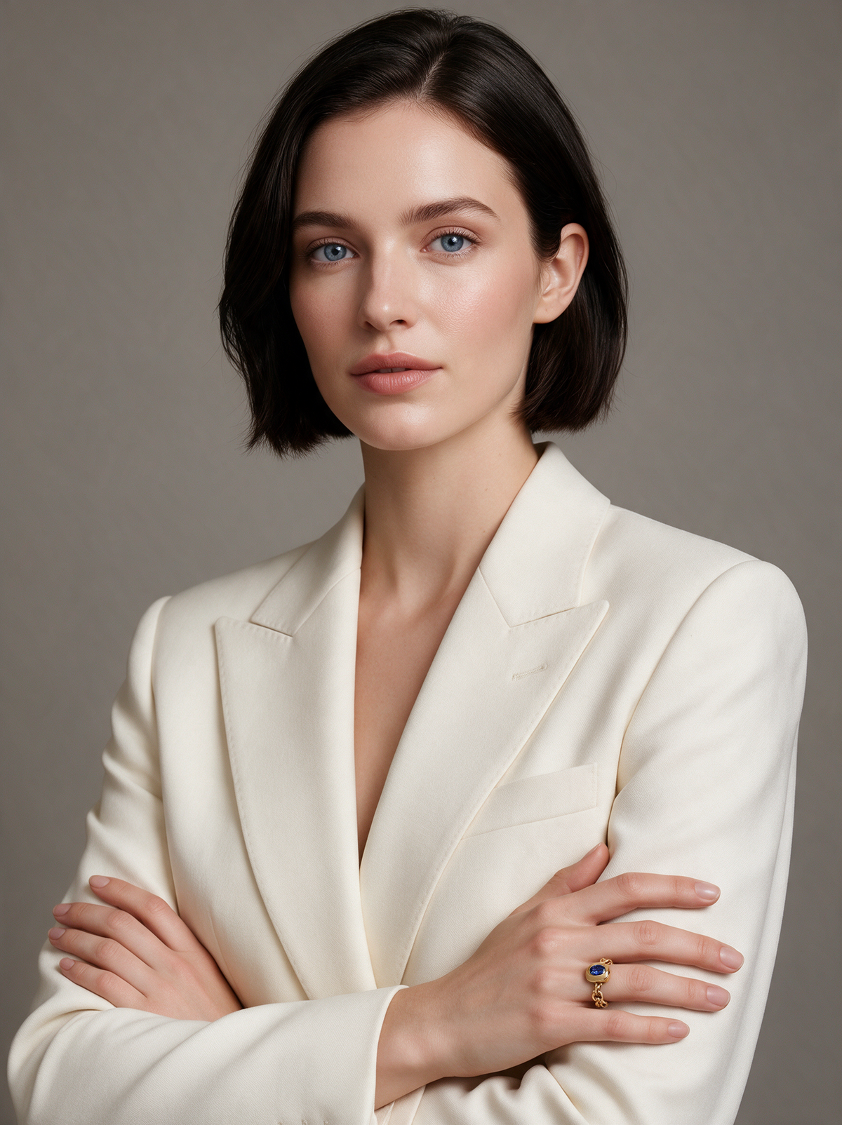 Model in an ivory blazer, arms folded, wearing the Chain Ring in 18K gold vermeil with a blue stone