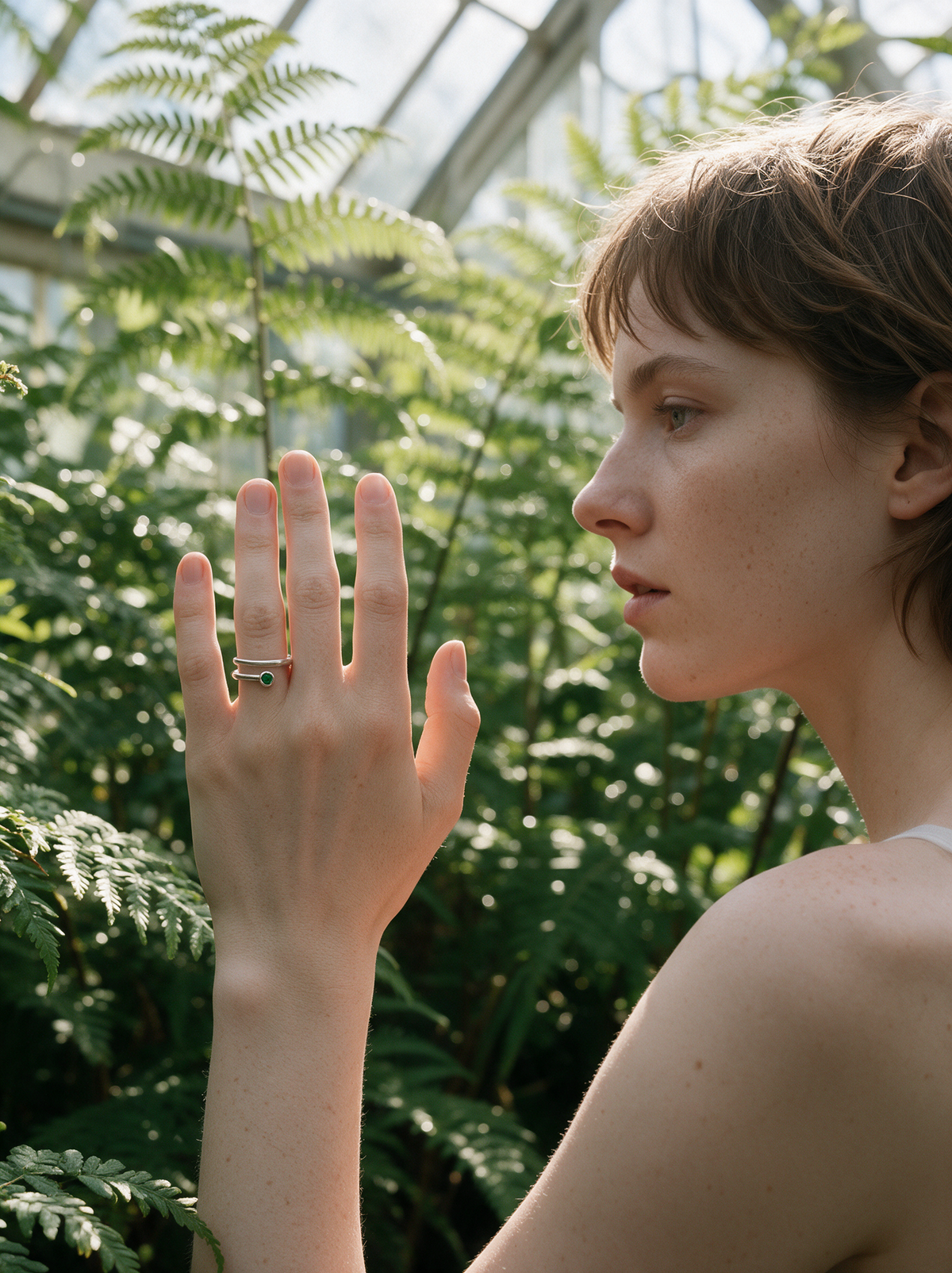 Model among greenhouse ferns wearing the Coil Ring in sterling silver with a green stone