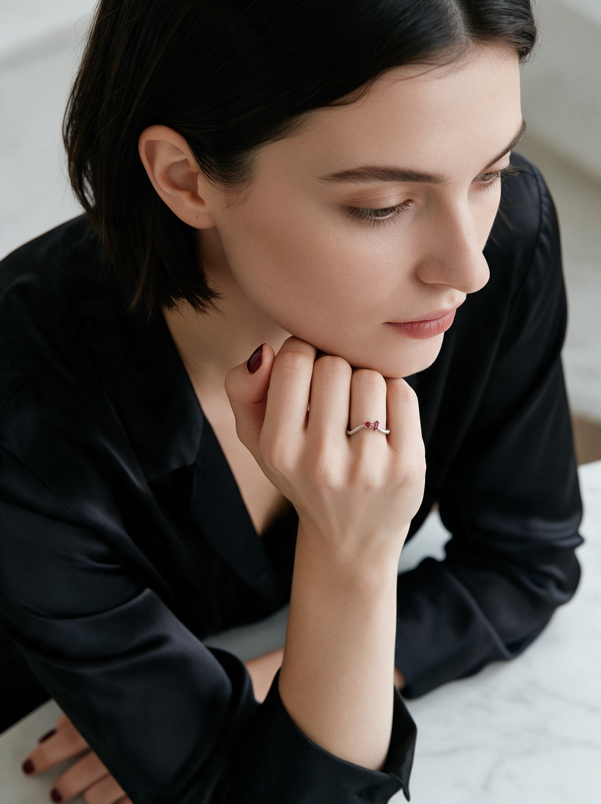 Model in black satin, chin on her hand, wearing the Dot Dash Ring in sterling silver with red stones