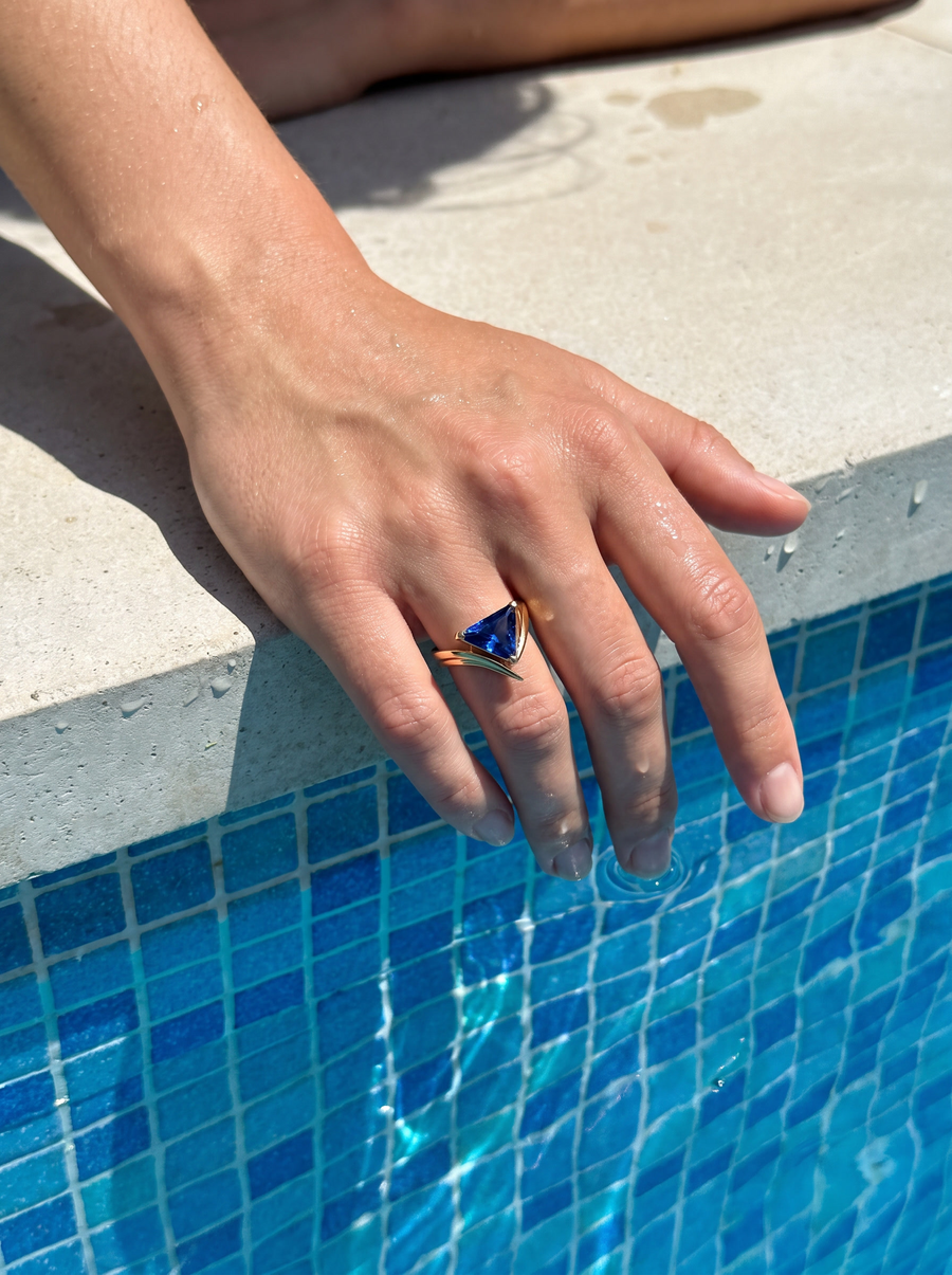 V-Ring in 18K gold vermeil with a blue stone on a hand resting at the edge of a tiled pool