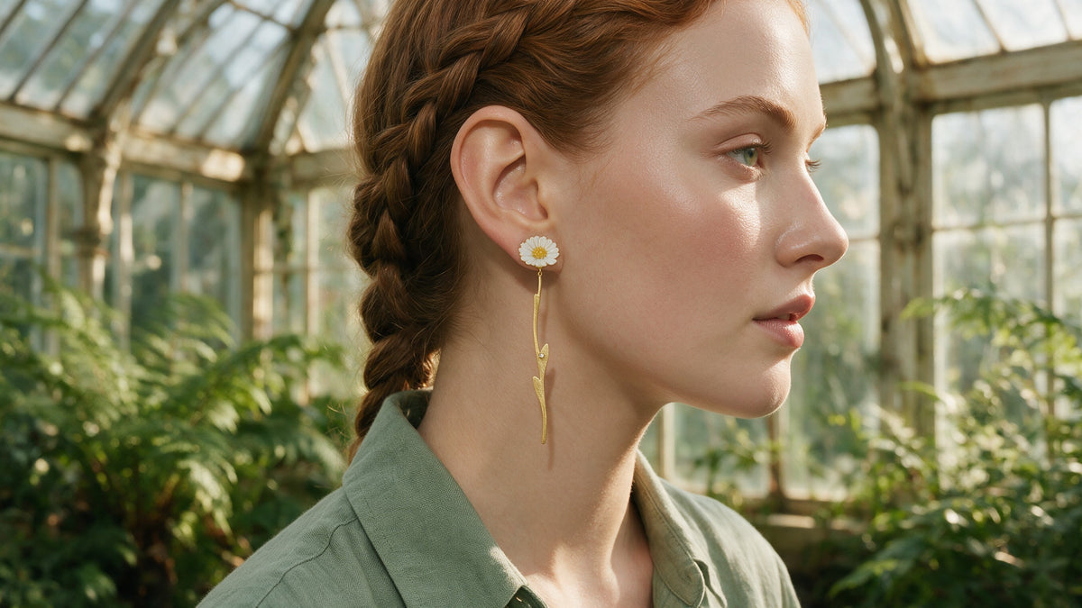 Qilver daisy stem drop earring in gold, worn in a sunlit greenhouse