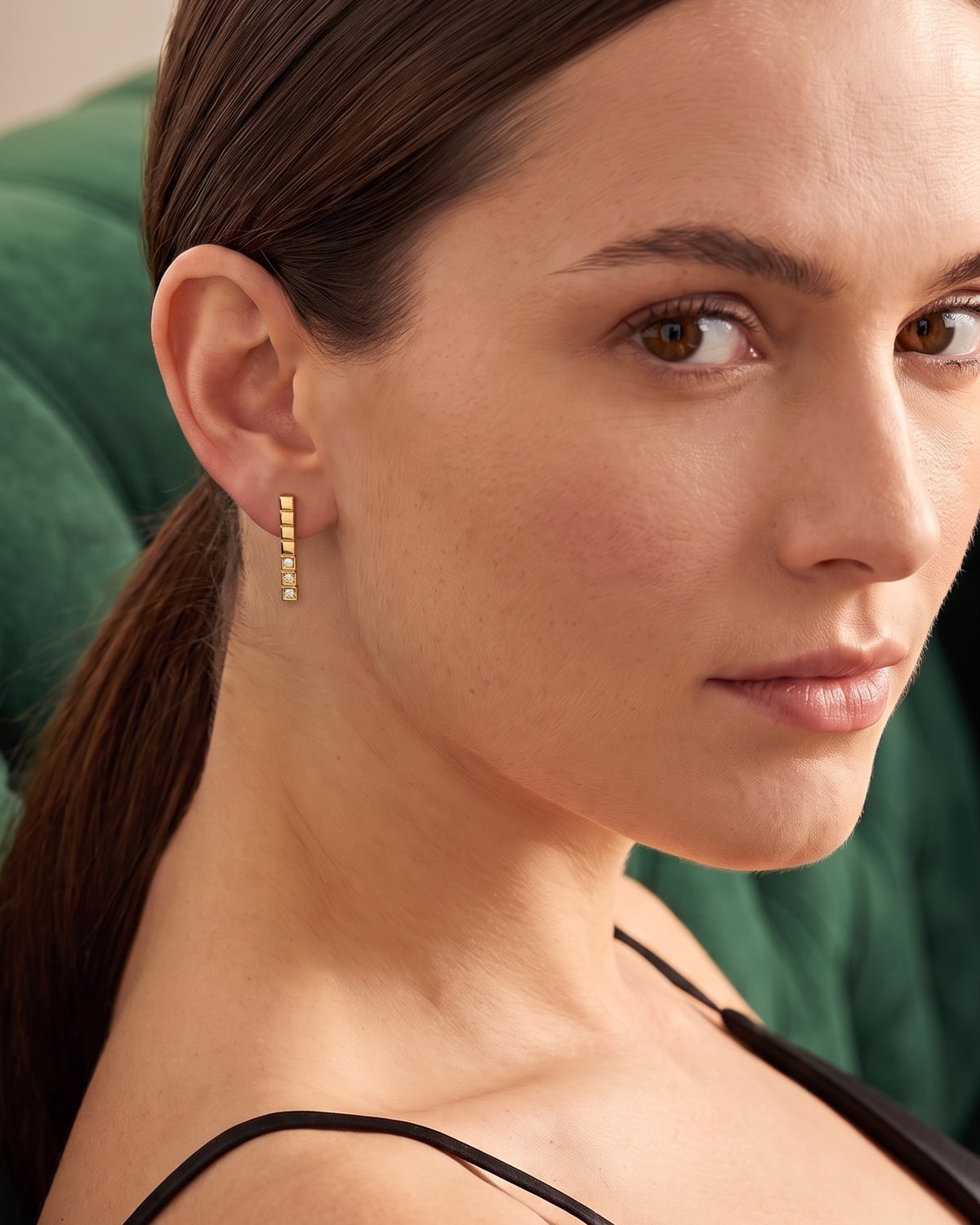 Model wearing the Stacked Cube Earrings in 18K gold vermeil, looking over her shoulder on a green velvet sofa