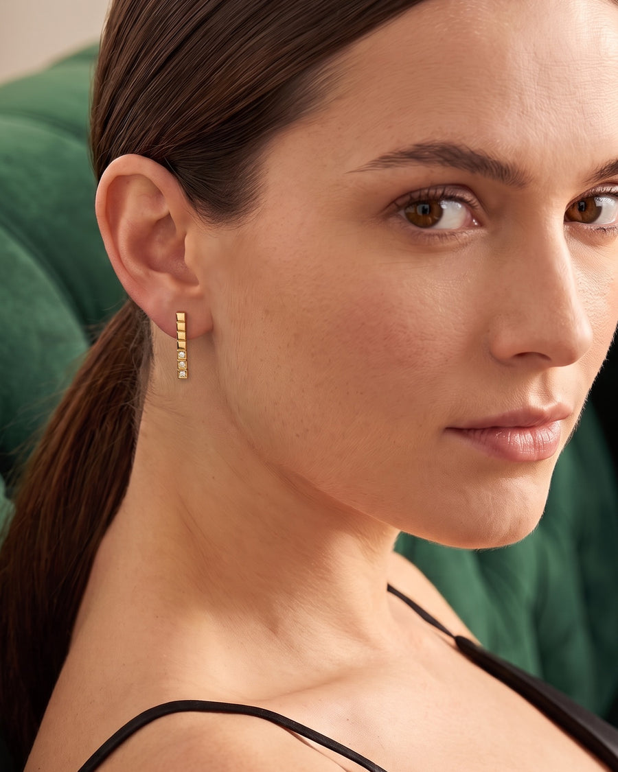 Model wearing the Stacked Cube Earrings in 18K gold vermeil, looking over her shoulder on a green velvet sofa