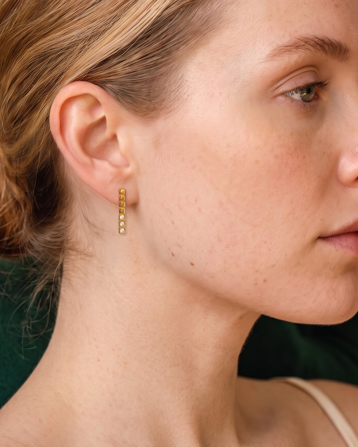 Model wearing the Stacked Cube Earrings in 18K gold vermeil, in profile against a green velvet sofa